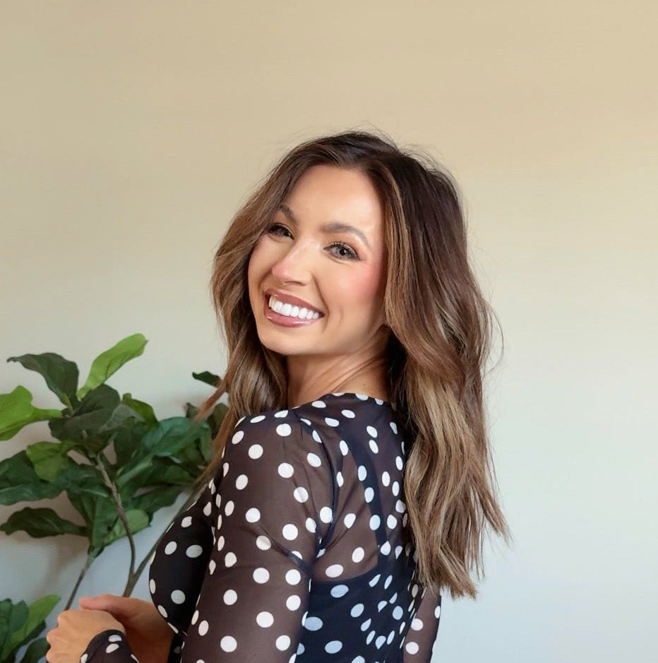 Woman wearing a black dress with white polka dots indoors next to a plant.
